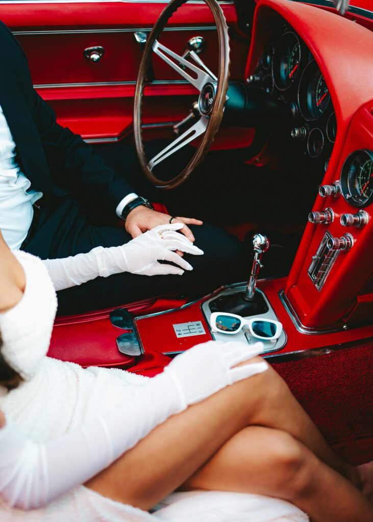 Image of engaged couple holding hands in red car.